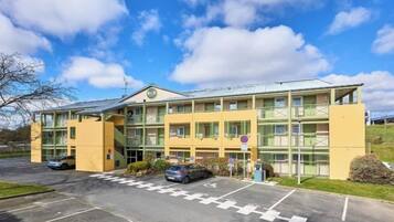 A two-story building with a flat roof, large windows, and a parking lot in front.