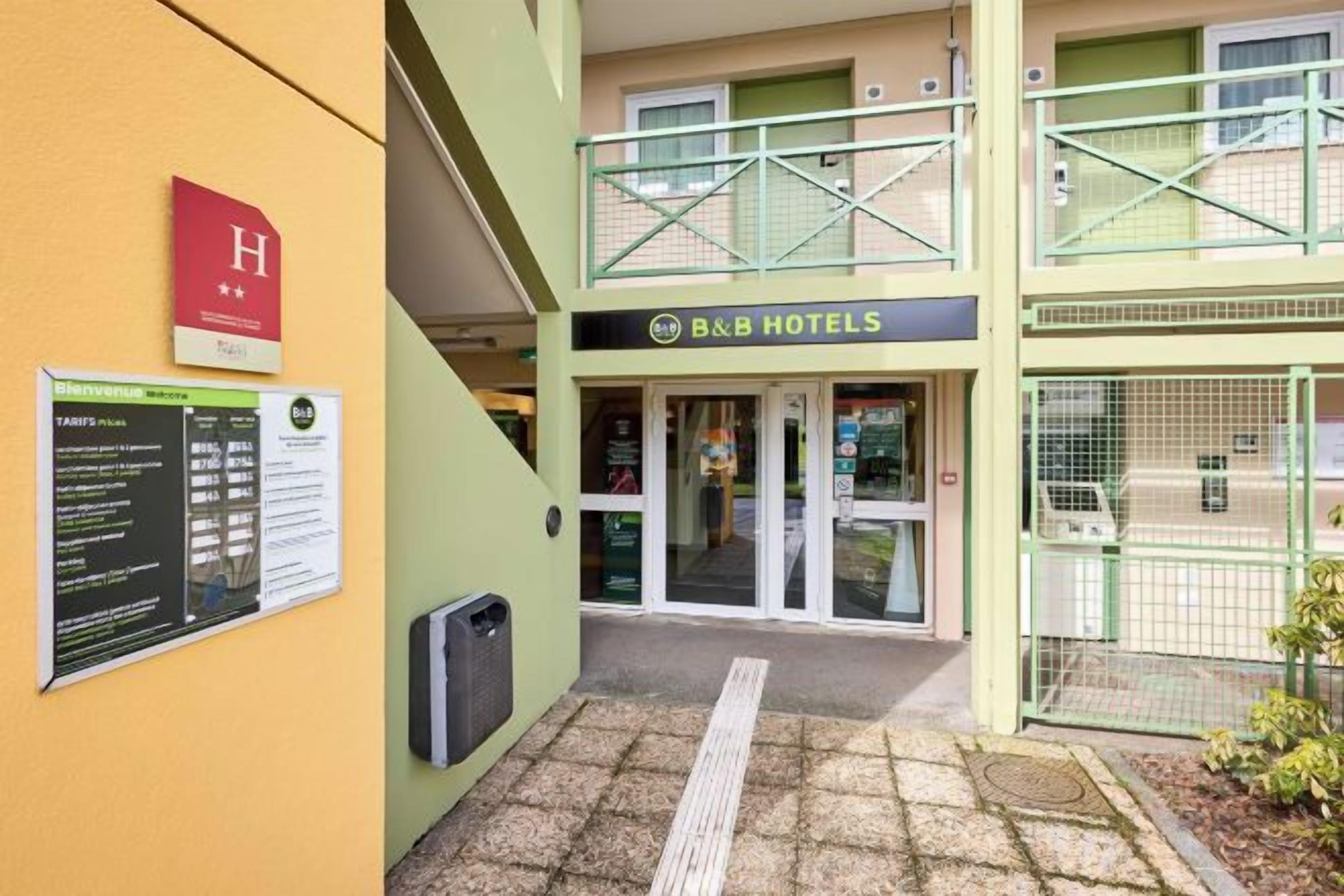 A hotel entrance with a double-height balcony, a sign for B&B Hotels, and a wheelchair-accessible ramp.