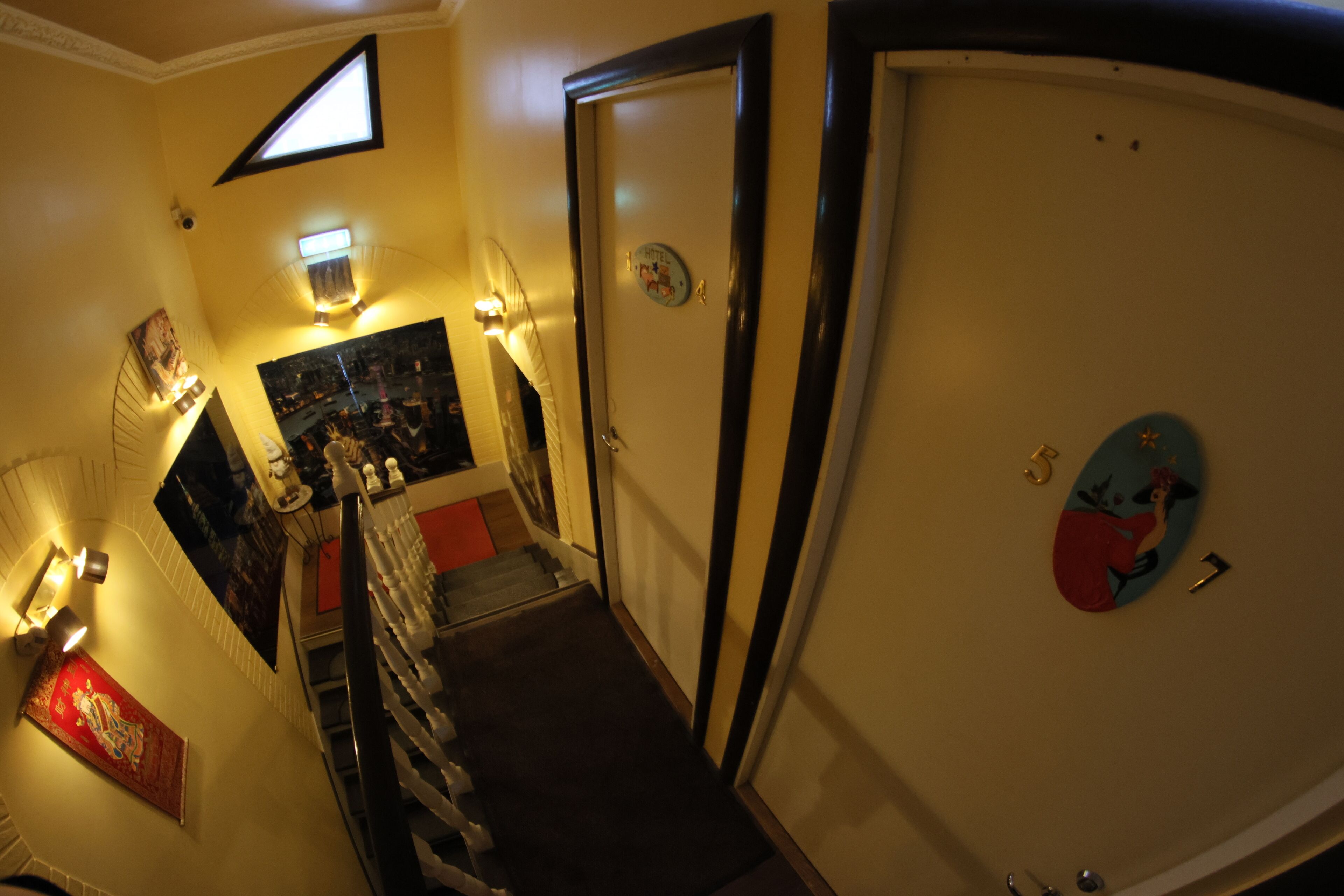 A narrow hallway with a staircase, a door with a decorative plate, and a wall-mounted light fixture.