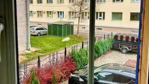 Une vue depuis une fenêtre donnant sur un quartier résidentiel, avec un immeuble à plusieurs étages, une voiture verte et une boîte aux lettres indiquant les tarifs postaux.