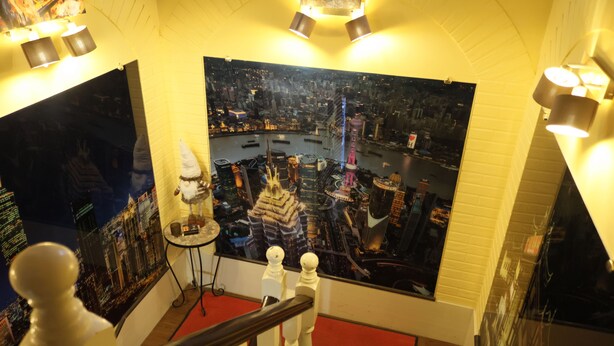 Une pièce décorée d’un grand tableau représentant un paysage urbain, d’une statue blanche et d’un tapis rouge.