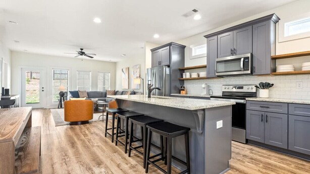 Una cocina moderna con una isla central, taburetes de bar y un comedor con mesa de madera.