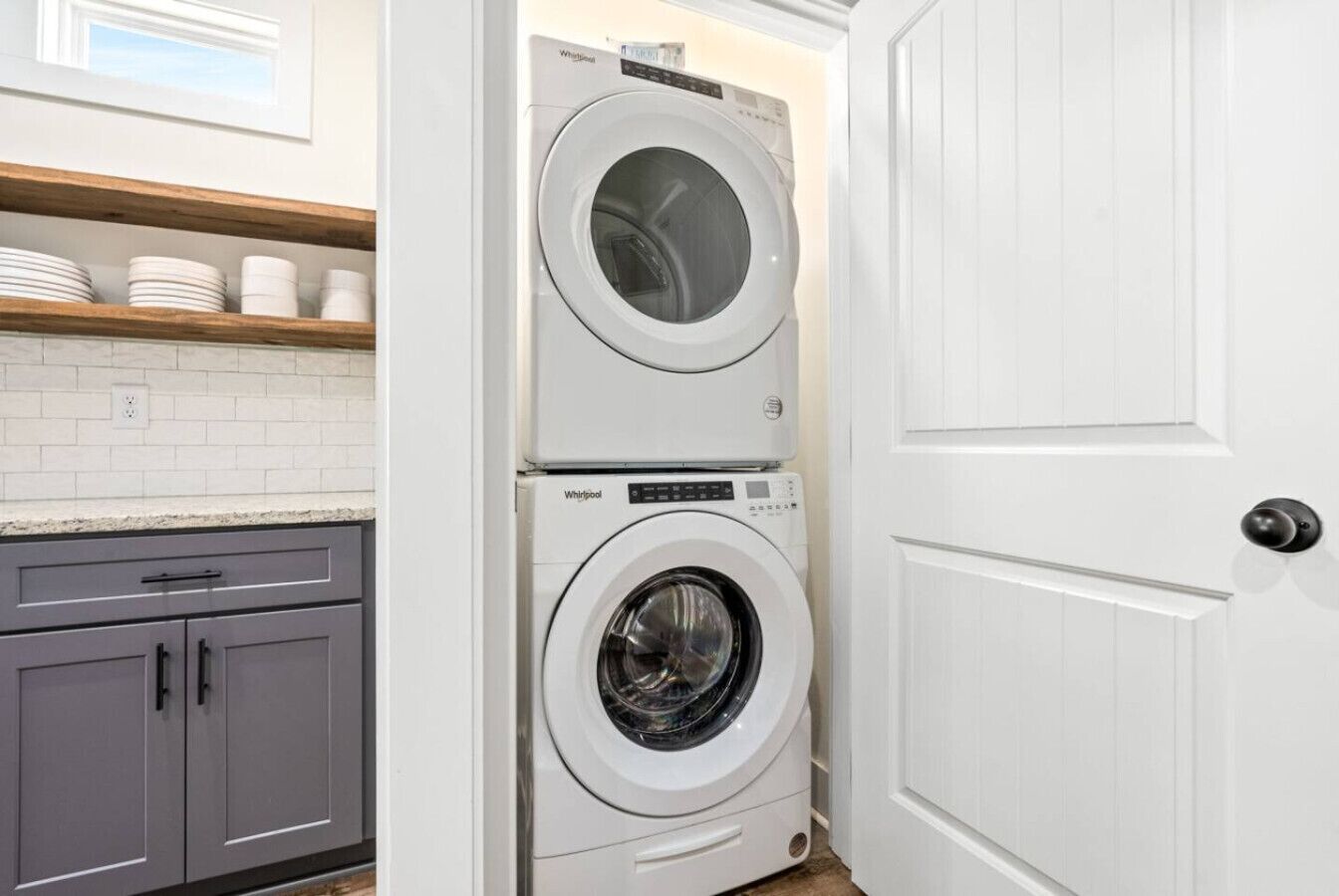 Ein Waschraum mit zwei übereinander gestapelten Whirlpool-Waschmaschinen, einer Holzablage mit weißen Tellern und einem grauen Schrank.