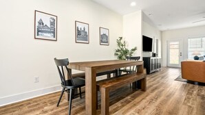 Un comedor moderno con una mesa y sillas de madera, cuadros en la pared y un televisor al fondo.