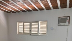 A bedroom with two beds, a window with blinds, an air conditioning unit, and tiled flooring.