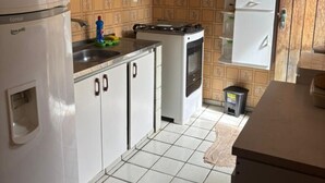 A compact kitchen with white cabinets, a refrigerator, a stove, and a small trash bin.