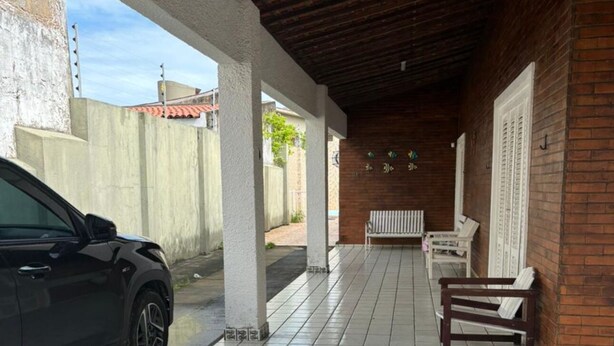 A covered parking area with a car, tiled floor, benches, and a brick wall.