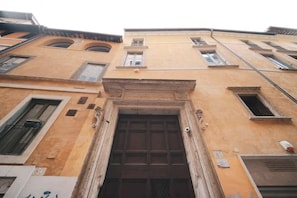 Une façade d’immeuble avec une entrée centrale, de nombreuses fenêtres et une porte bien visible.