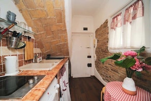 Une cuisine étroite avec un mur en briques, une porte blanche et une fenêtre ornée de rideaux à carreaux.