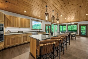 A spacious kitchen with wooden cabinets, a large island with bar stools, and multiple windows offering views of the outdoors.