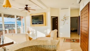 A modern living room with a large TV, a ceiling fan, and a view of the mountains through large windows.