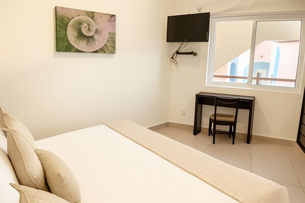A bedroom with a bed, a desk, a chair, a TV, and a window with a view of buildings. - Stunning Ocean View! (Bajos de Chila)