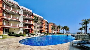 A hotel with a swimming pool, multiple balconies, and palm trees.