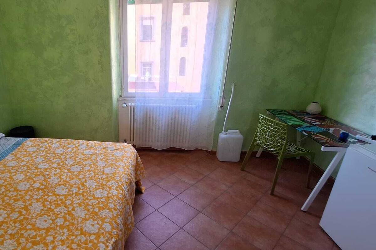 Una habitación pequeña con cama, escritorio, silla y radiador.