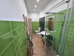 Une salle de bain avec des carreaux verts, une douche en verre, des toilettes et un lavabo.
