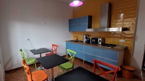 A compact kitchen with a dining area, featuring a small table and colorful chairs, a blue cabinet, and a modern stove. - DOMUS BAIANO  (Naples)
