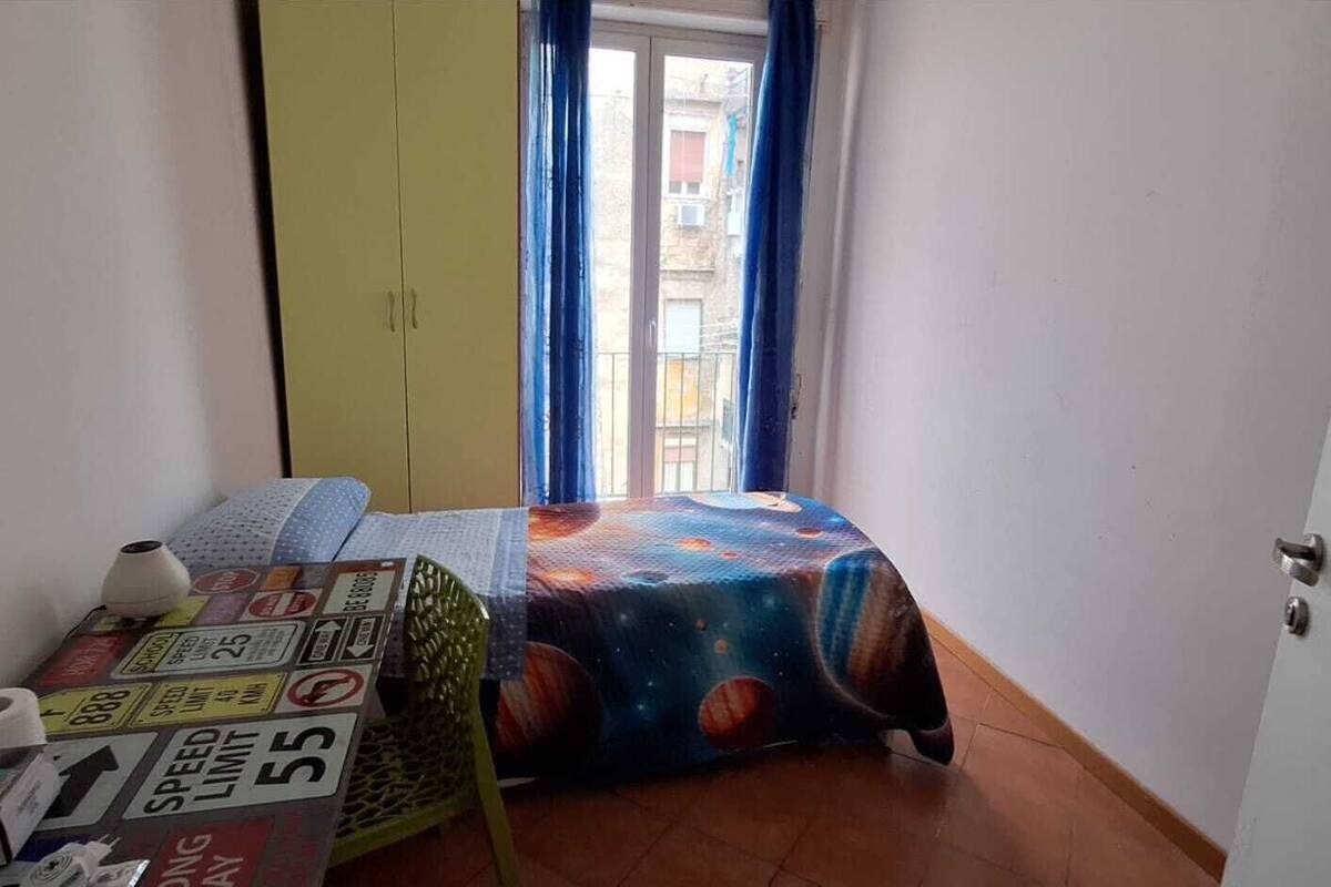 Una habitación pequeña con cama, puerta y ventana con cortinas.