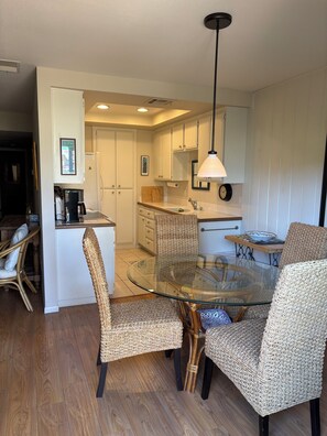 A compact kitchen with white cabinets, a round glass dining table, wicker chairs, and a hanging pendant light. - 3 Bedroom Ground Floor Unit in Palm Desert (Palm Desert)