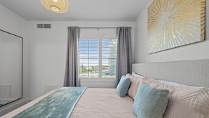 Quarto com cama, janela com cortinas, uma obra de arte na parede e luminária no teto.