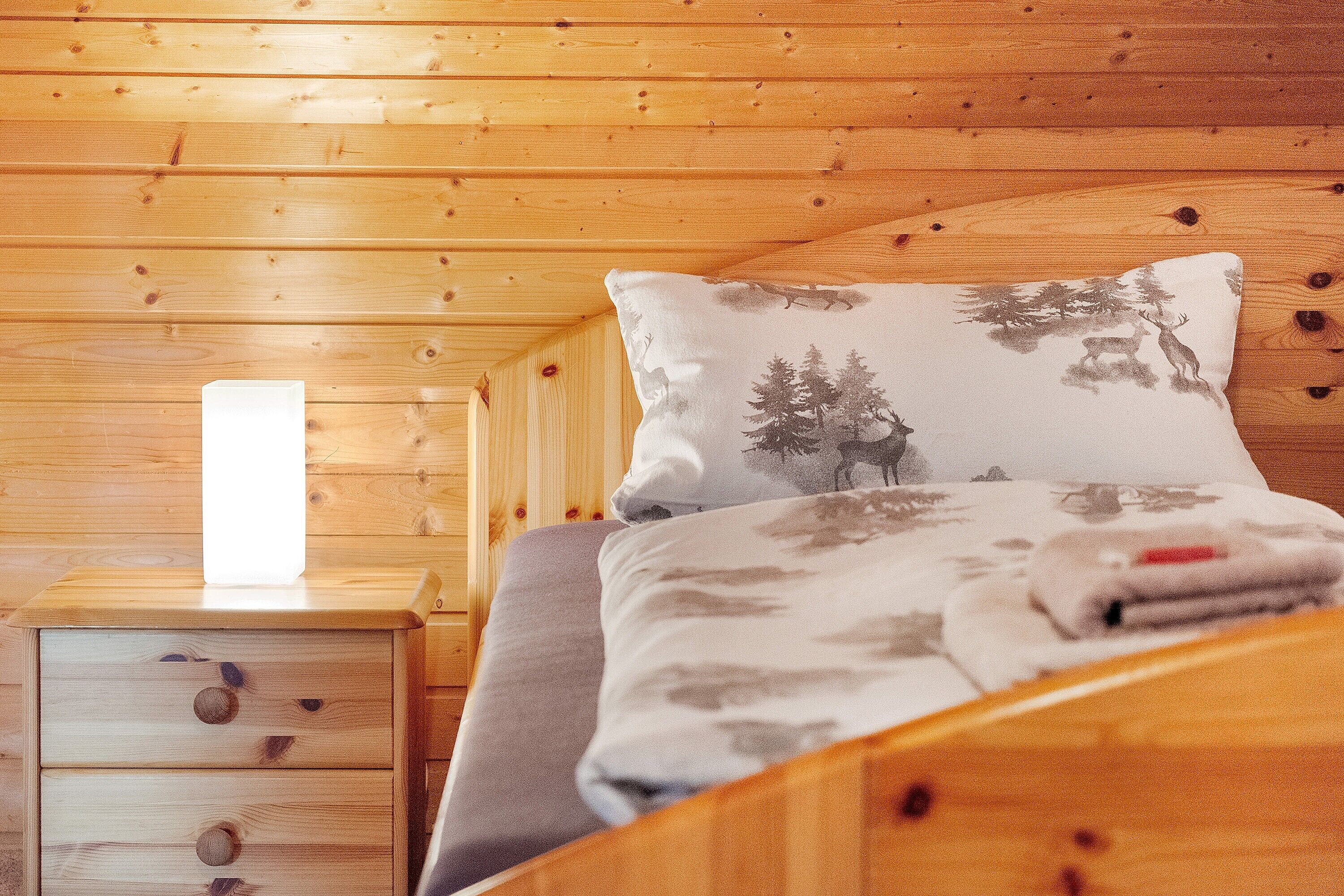 A wooden cabin-style room with a bed, a nightstand, and a drawer unit.