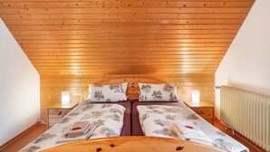 A bedroom with a wooden ceiling, two beds with matching pillows, bedside lamps, and a radiator. - 'Elzblick' Apartment with Shared Pool, Garden, and Wi-Fi (Elzach)
