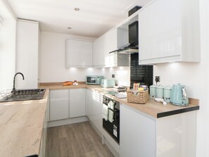 Una cocina moderna con armarios blancos, encimera de madera, microondas, tostadora y hervidor.