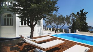 Eine Holzterrasse mit Pool, Liegestühlen und Blick auf das Meer und die Bebauung.
