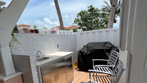 Un espace extérieur aménagé avec un barbecue, un évier, une chaise et un sol carrelé.