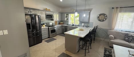 A modern kitchen with stainless steel appliances, a central island with bar stools, and a dining area with a sofa and coffee table.