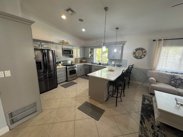 Una cocina moderna con electrodomésticos de acero inoxidable, una isla central con taburetes de bar y una zona de comedor con sofá y mesa de centro.