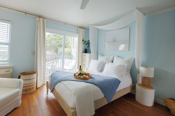 A bedroom with a bed, a bedside table, a lamp, a wicker basket, and a window with curtains.