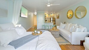 A hotel room with a bed, a white sofa, a dining area with stools, and a kitchen in the background. - 30A Gem • Steps to Sand • Balcony Sunsets • Pool (Inlet Beach)
