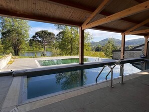 A swimming pool with a wooden deck and a view of a lake and mountains.