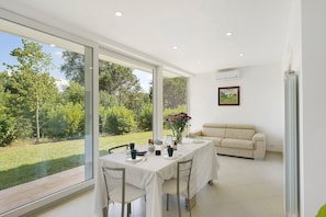 A dining area with a table set for four, a sofa, and a large window offering a view of a garden. - Apartment 1 with Lake View (Alvignano)