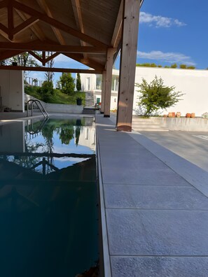 A swimming pool with a wooden deck, a metal ladder, and a clear sky.
