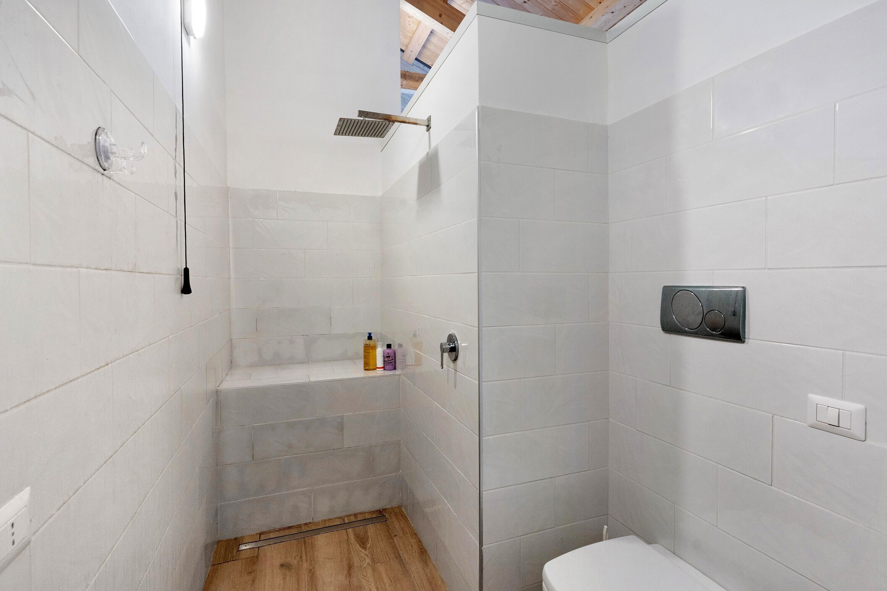 Ein modernes Badezimmer mit weißen Fliesen, einer Dusche, einer Toilette und einem kleinen Ablagefach für Toilettenartikel.