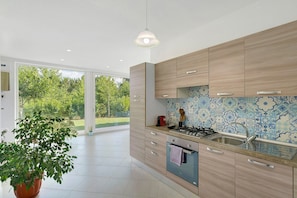 A modern kitchen with wooden cabinets, a gas stove, and a large window offering a view of greenery. - Apartment 1 with Lake View (Alvignano)