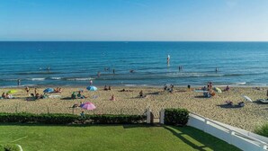 A beach with people sunbathing and swimming, a clear sky, and a fence in the foreground. - Beach House in front the sea (Marbella)