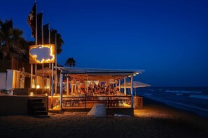 Un restaurant situé en bord de mer, doté d’une terrasse couverte, d’une grande enseigne lumineuse et de plusieurs drapeaux.