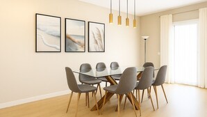 A dining area with a glass table surrounded by six chairs with wooden legs. There are three framed artworks on the wall above the table. - Beach House in front the sea (Marbella)