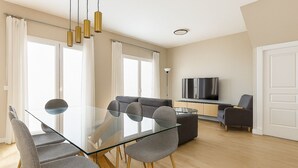 A modern living room with a glass dining table, grey upholstered chairs, a grey sofa, and a flat-screen TV on a wooden cabinet. - Beach House in front the sea (Marbella)