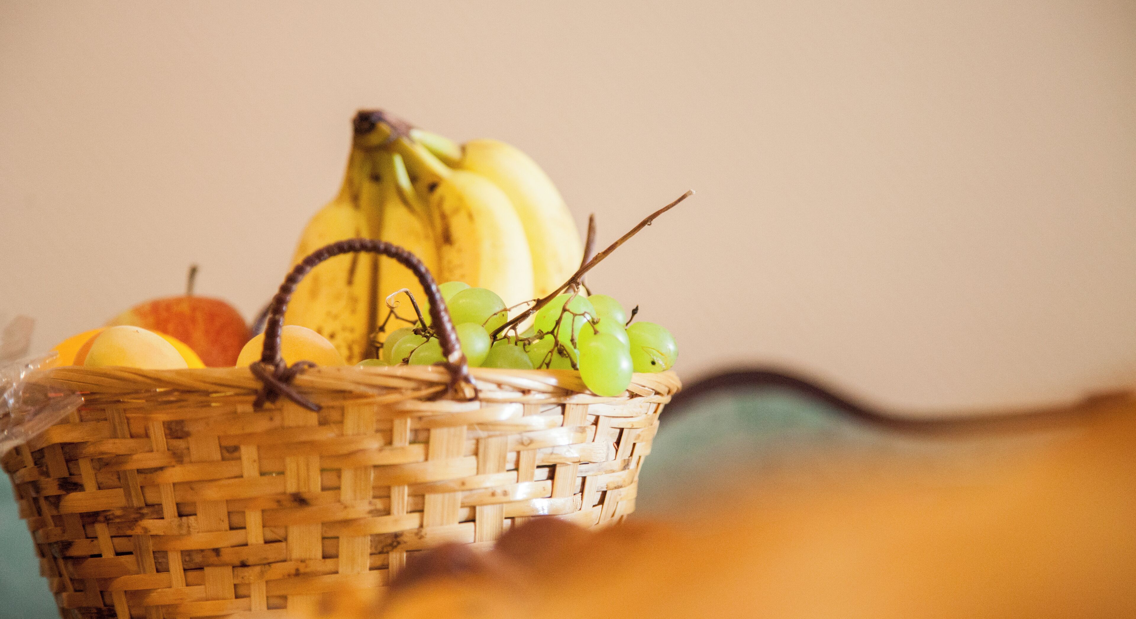 Una cesta de mimbre con plátanos, uvas y una manzana.