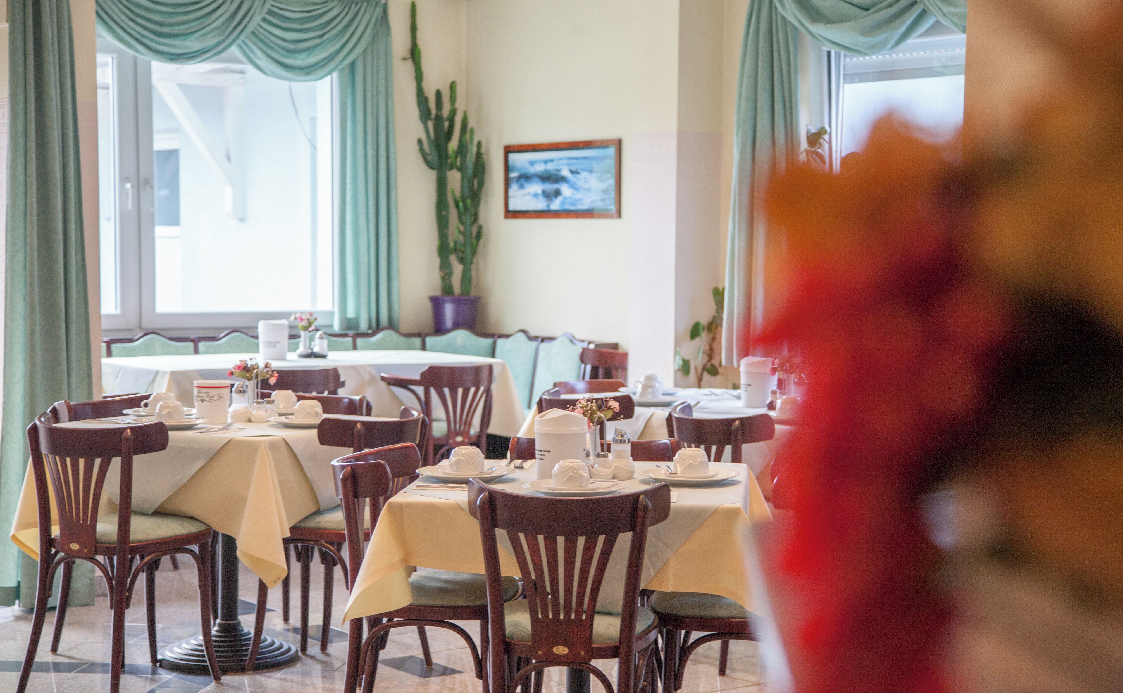 A dining area with tables set for service, chairs, and a large window with curtains.