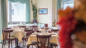 A dining area with tables set for service, chairs, and a large window with curtains.