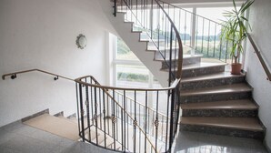 A spiral staircase with a metal railing, leading to a landing with a potted plant. - Five Studios - Premium Rooms (Ramstein-Miesenbach)