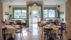 A restaurant with multiple tables and chairs, a central doorway, and large windows with curtains. - Five Studios - Premium Rooms (Ramstein-Miesenbach)