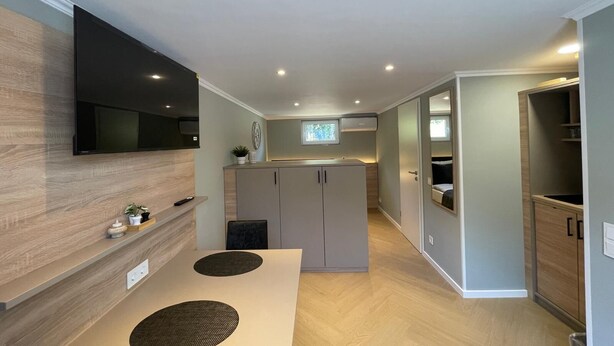 A modern kitchen with a flat-screen TV, built-in cabinets, and a dining area with a table and chairs. - Five Studios - Premium Rooms (Ramstein-Miesenbach)