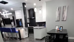 Una cocina moderna con una isla central, taburetes de bar, iluminación colgante y un comedor con mesa y sillas.