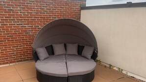 Un espacio de estar al aire libre con cojines, un muro de ladrillo y suelo de baldosas.