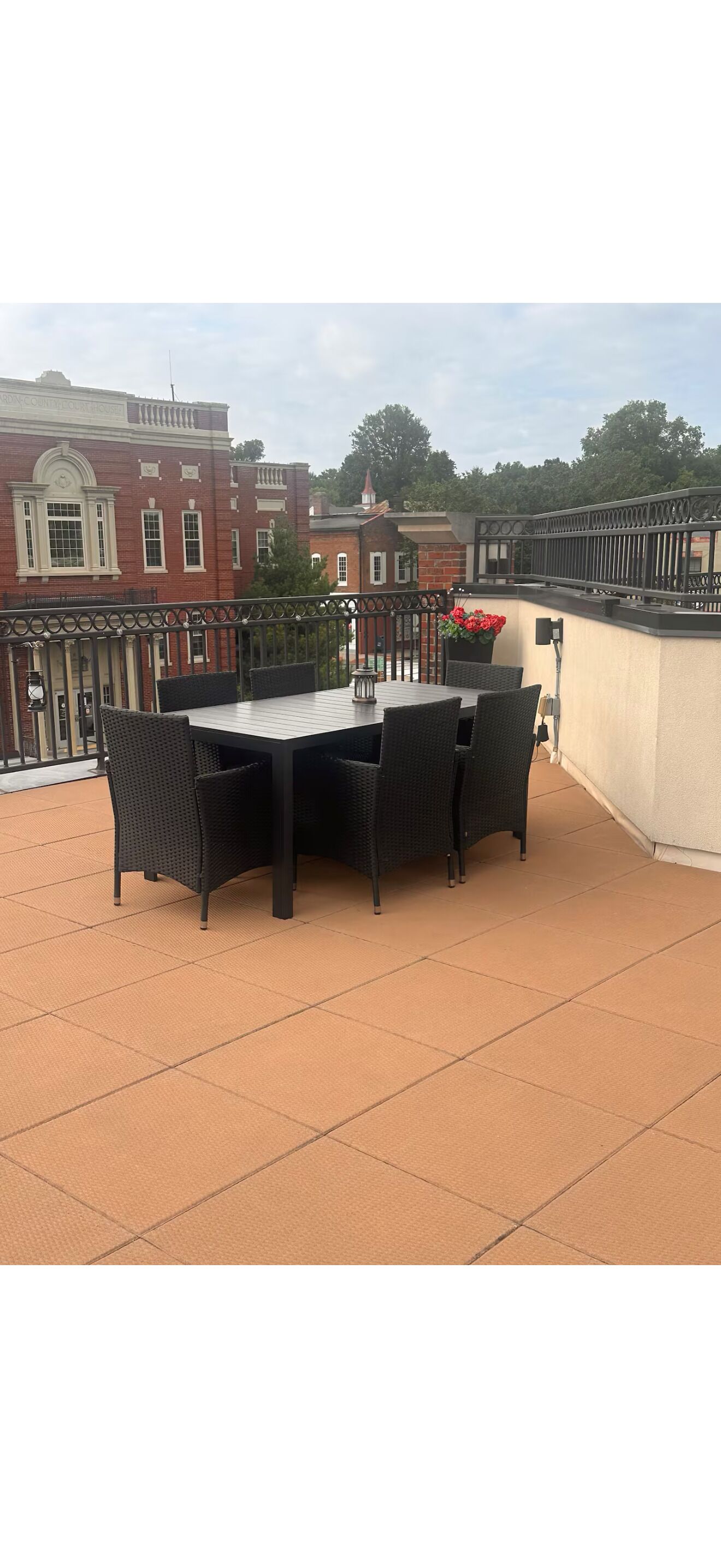 A rooftop terrace with a table and chairs, a potted plant, and a view of buildings.